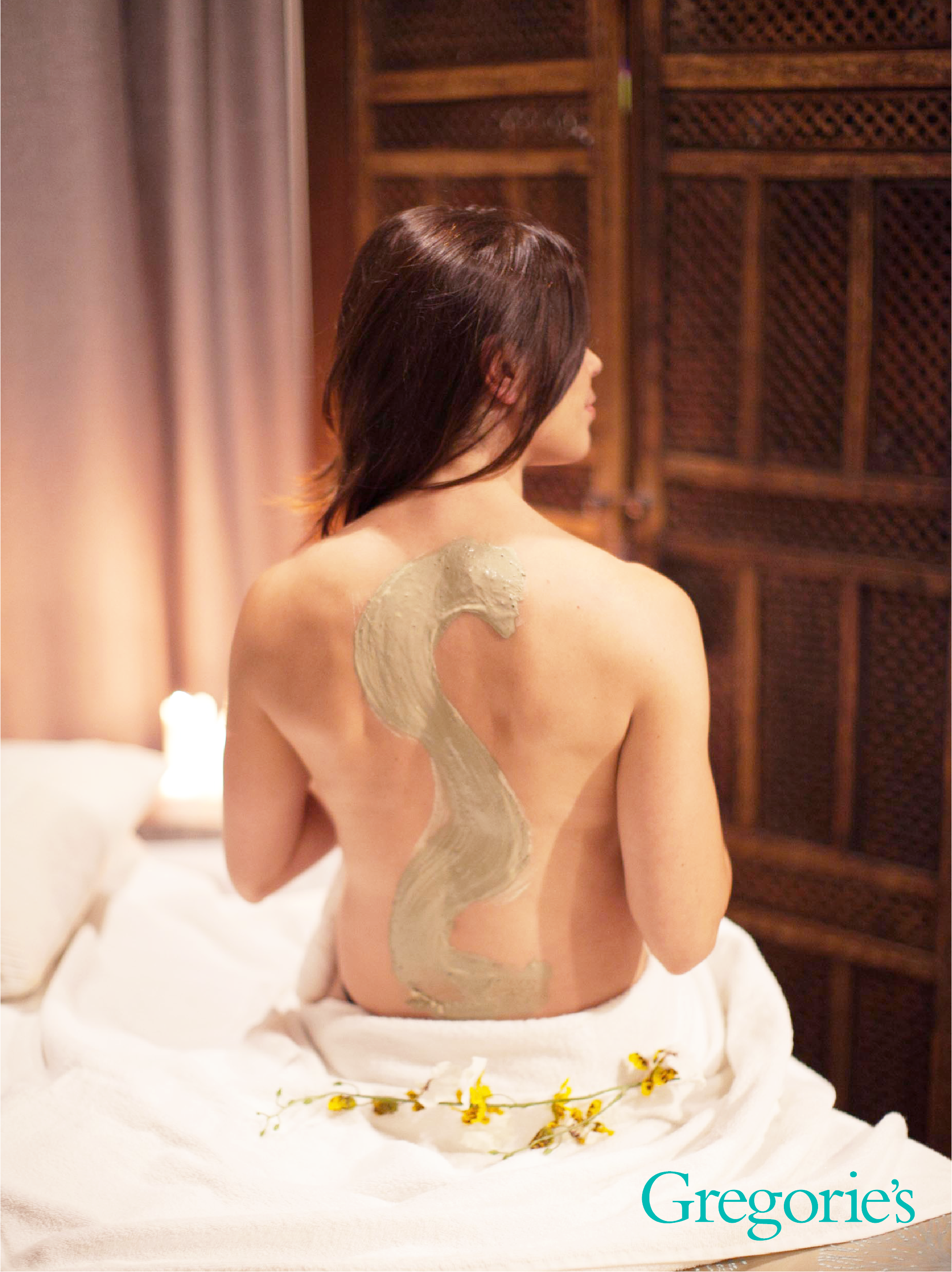 Woman sitting on massage table with mask on her back. Example of a body treatment.