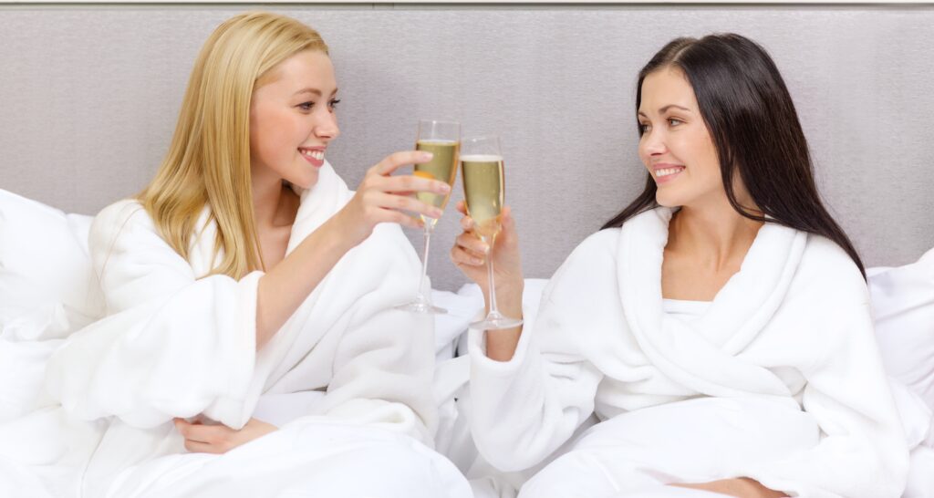 two women in white spa robes toast champagne