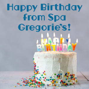 white birthday cake with rainbow sprinkles with candles that spell out happy birthday.  Candles are lit.  Text reads Happy Birthday from Spa Gregorie's!