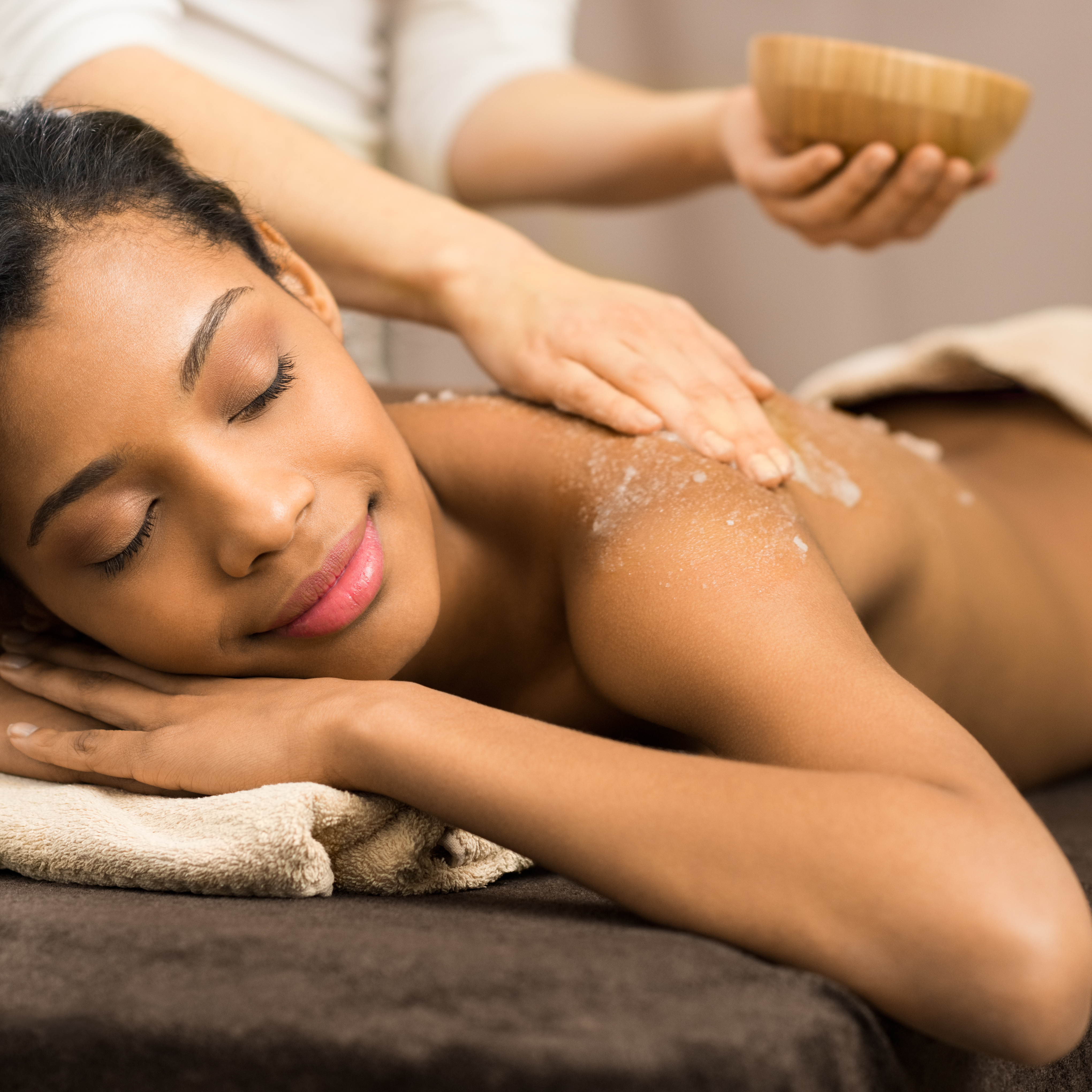 woman laying on massage table with eyes closed has scrub applied to her back